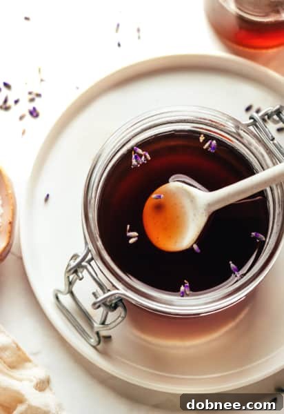 A glass of lavender syrup next to fresh lavender sprigs.