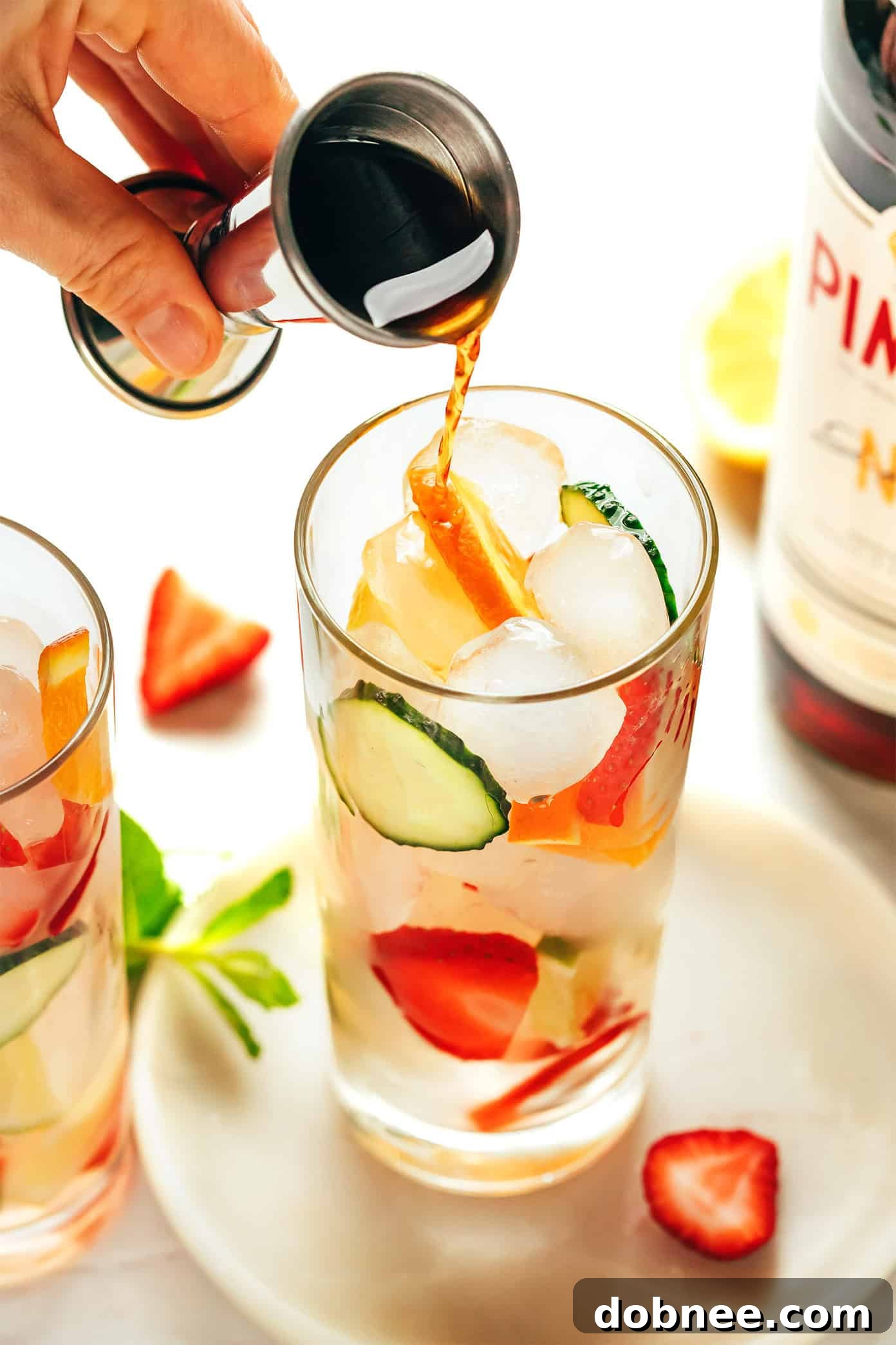 Ingredients for Pimm's Cup neatly arranged on a table, including Pimm's No. 1 bottle, lemon, cucumber, strawberries, and fresh mint.