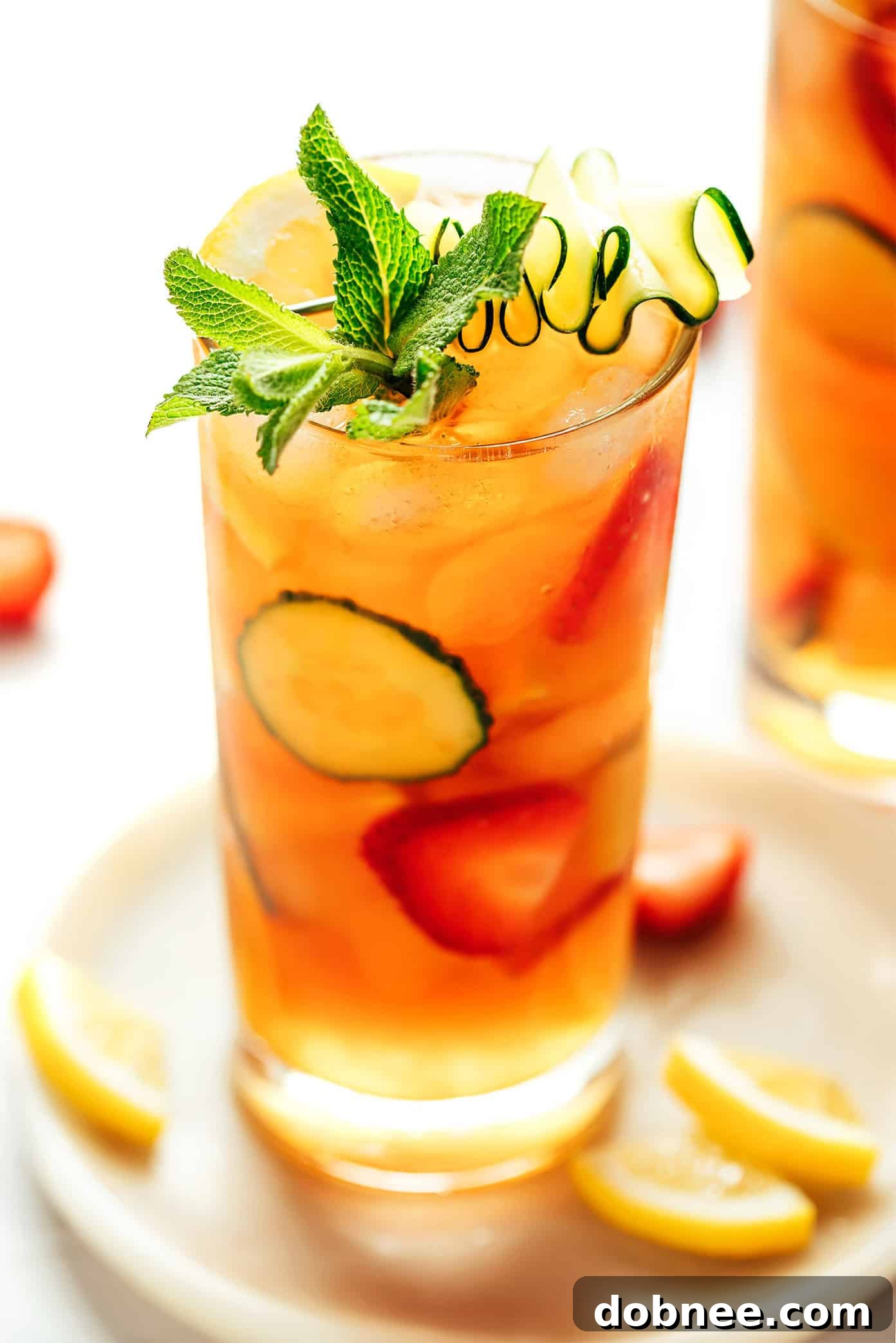 A glass of Pimm's Cup cocktail positioned next to a bottle of Pimm's No. 1, surrounded by an assortment of fresh fruits and herbs.