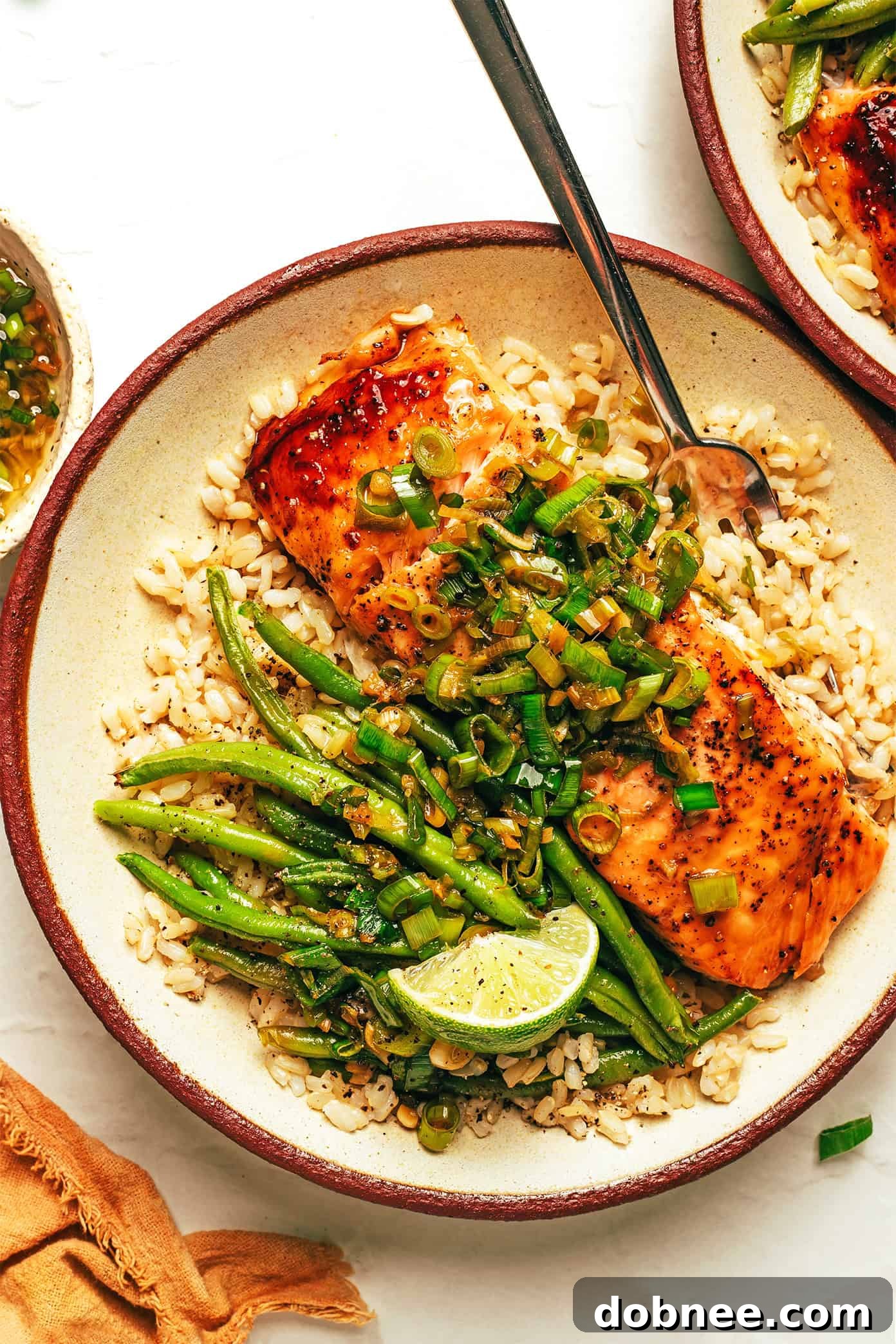 Two pieces of honey-roasted salmon with green beans on a white plate, drizzled with ginger scallion sauce.