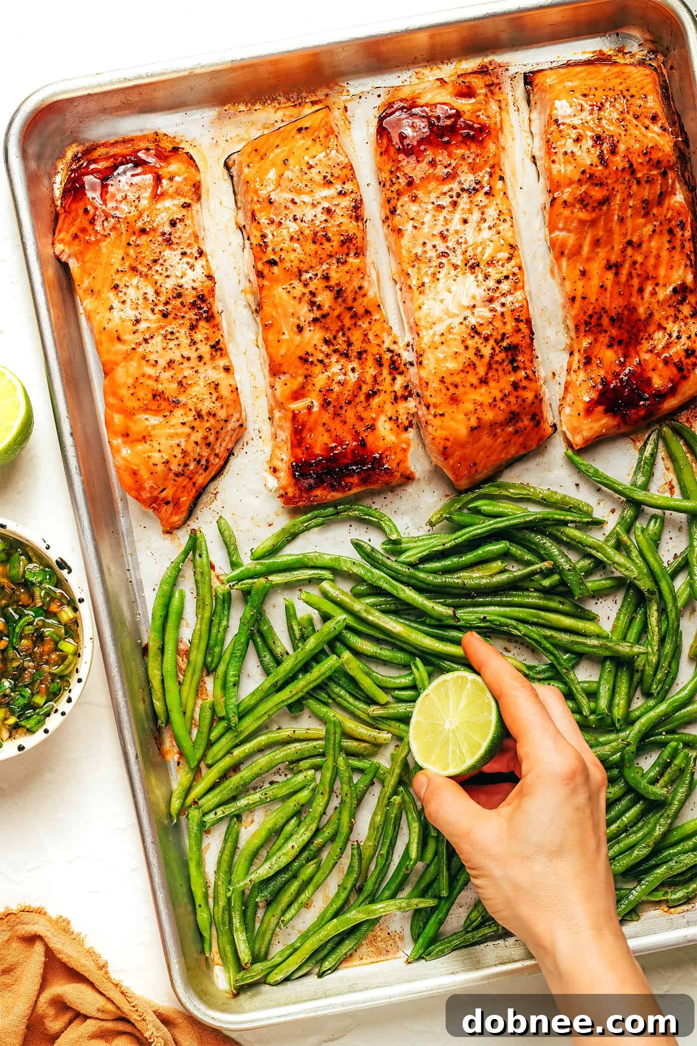 A vibrant bowl of honey-roasted salmon with green beans and rice, topped with a generous amount of ginger scallion sauce and fresh lime slices.