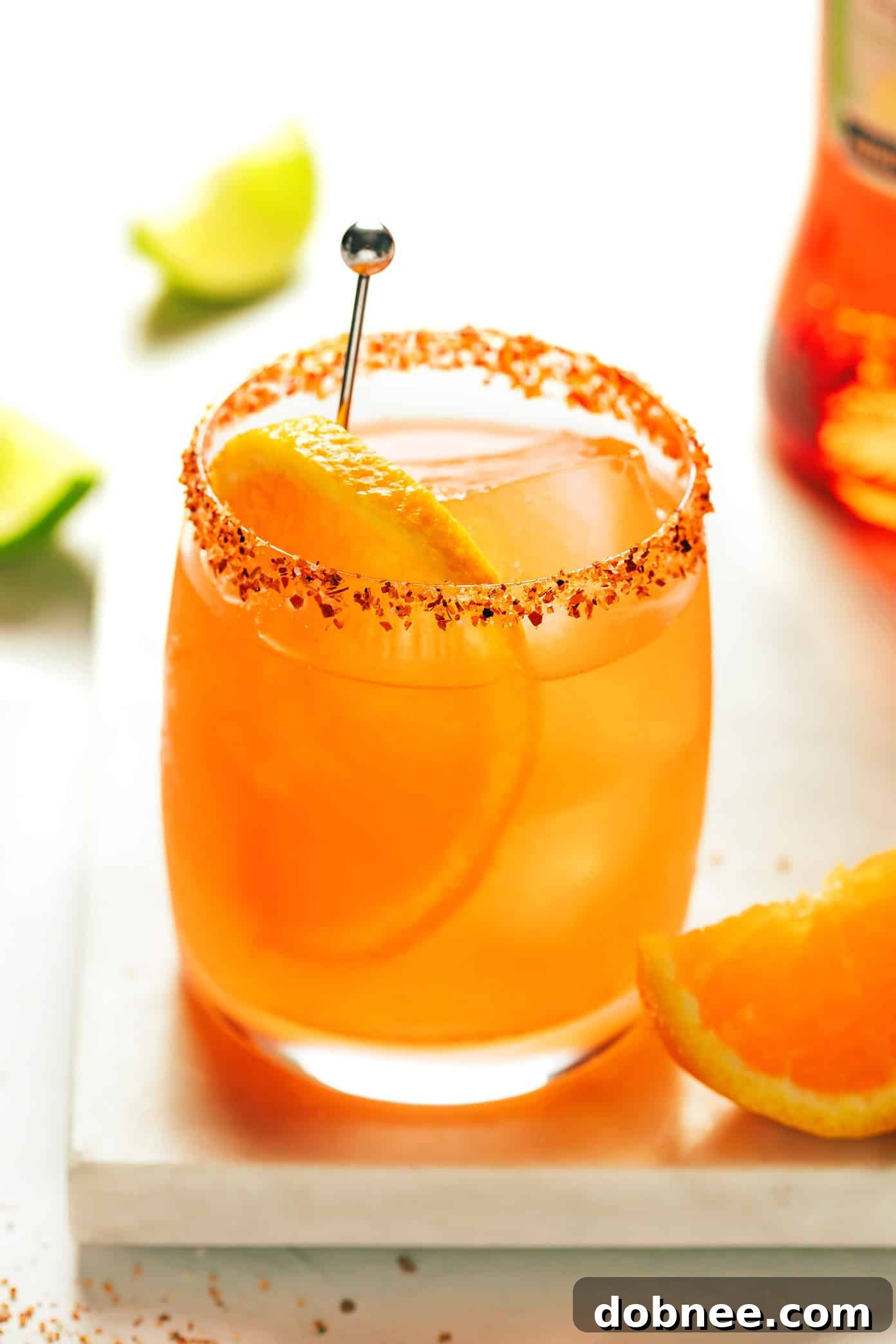 A close-up of a beautifully garnished Aperol Margarita, showing its vibrant color and Tajín rim.