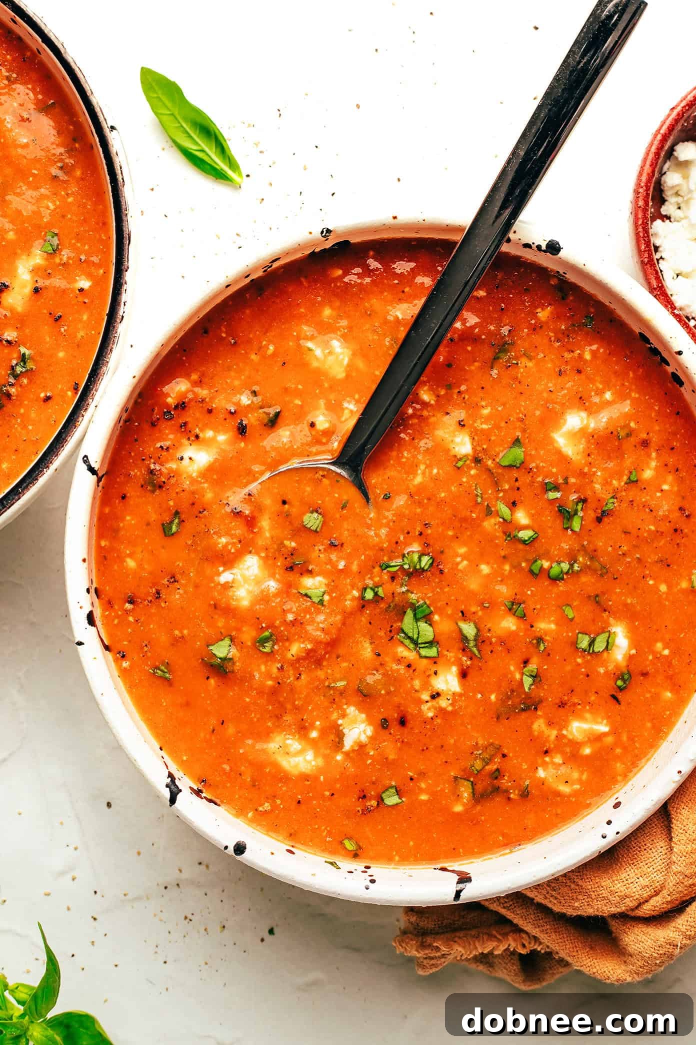 A bowl of tomato feta soup being served, with steam rising and fresh basil on top.