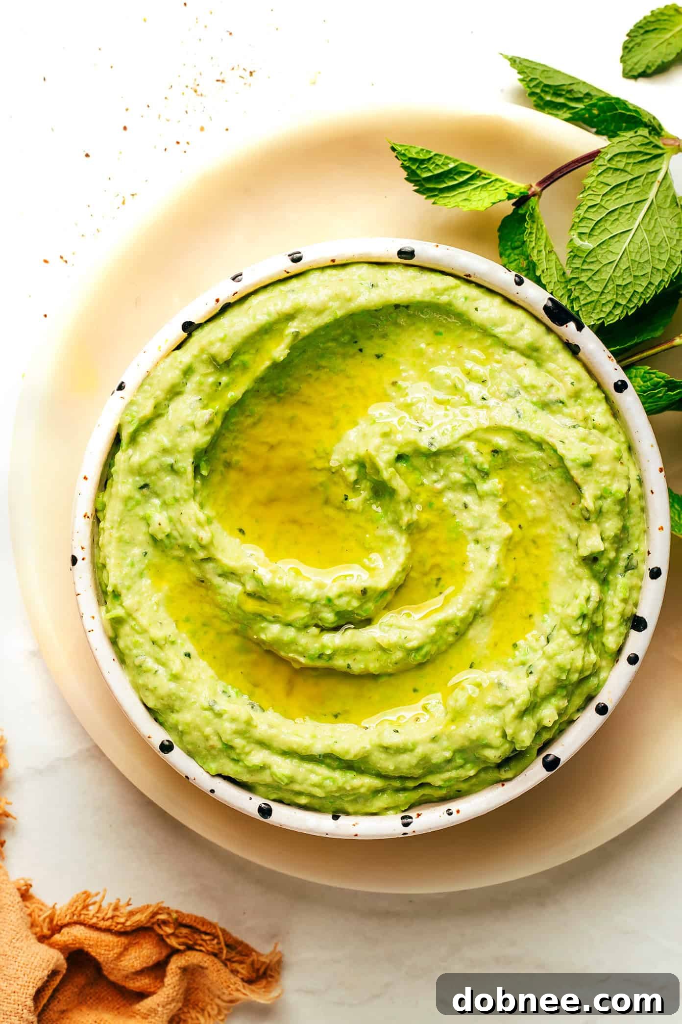 Vibrant Mint & Pea Hummus 5 Another perspective of the mint pea hummus in a bowl, with a spoon scooping a portion, showcasing its thick and creamy texture.
