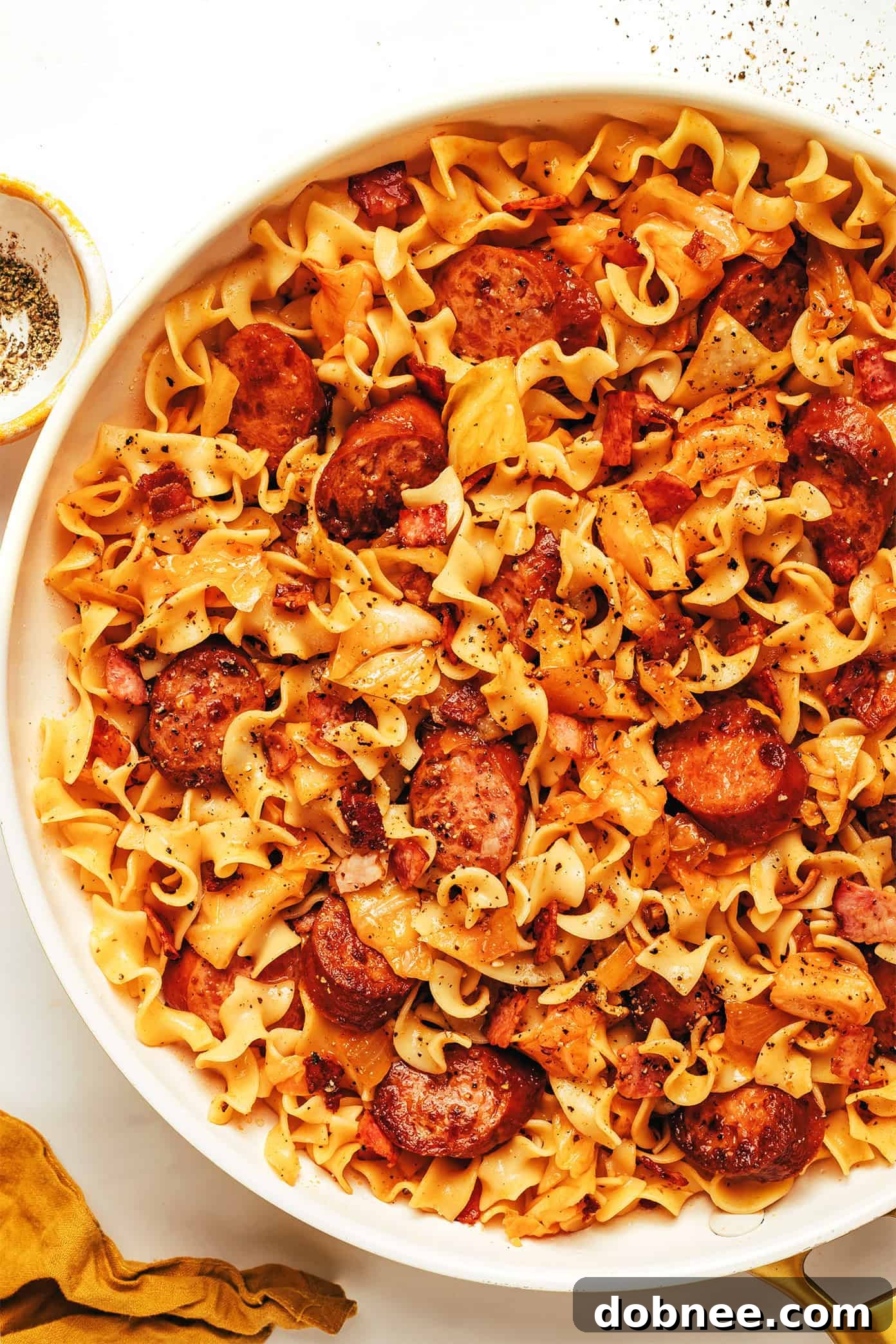 A beautifully plated serving of Kielbasa and Cabbage Noodles in a rustic white bowl, ready for enjoyment.