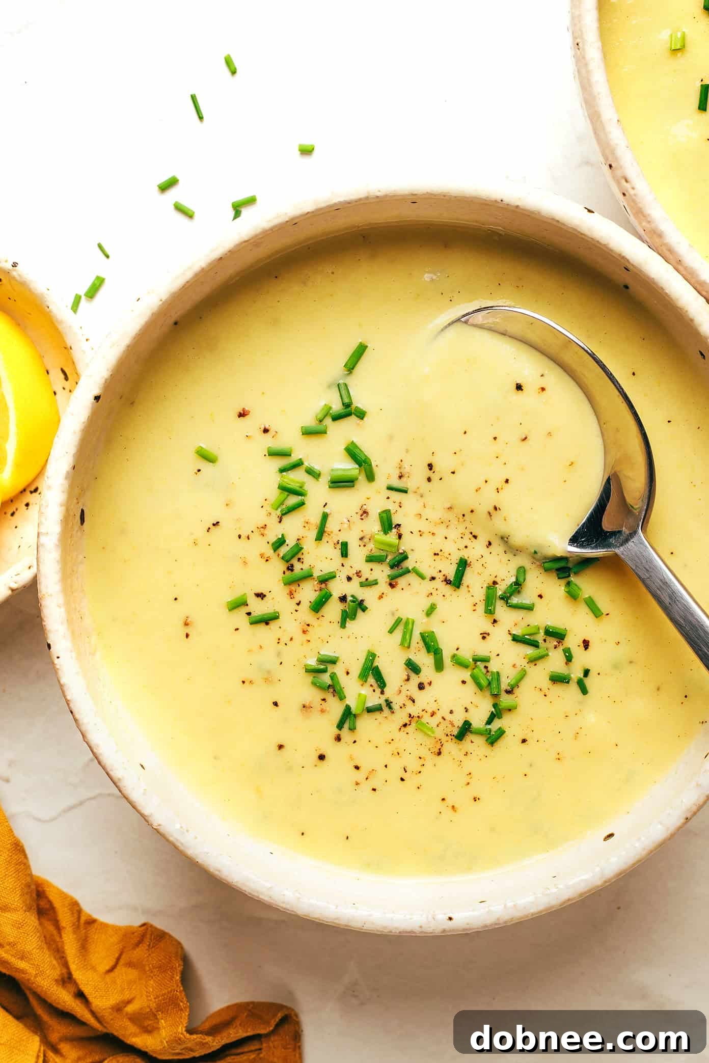 A bowl of creamy celery soup garnished with fresh chives, next to a rustic loaf of bread on a wooden surface.
