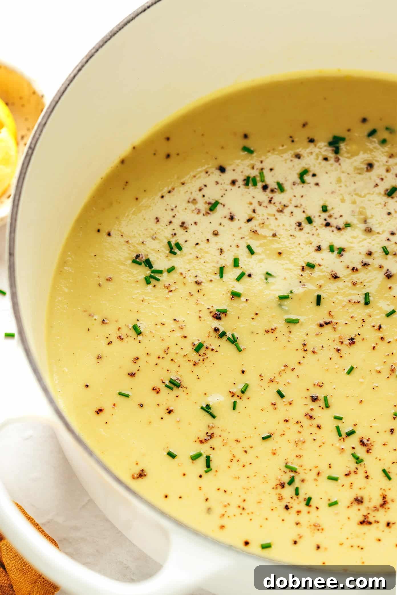 Four bowls of creamy celery soup, each garnished with fresh herbs, arranged on a rustic wooden table, with one bowl being dipped into with a spoon.