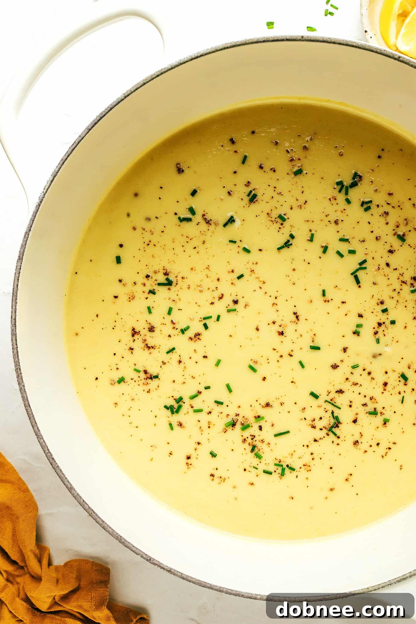 A top-down view of a rustic table setting with a large pot of creamy celery soup, surrounded by bowls, fresh bread, and ingredients.