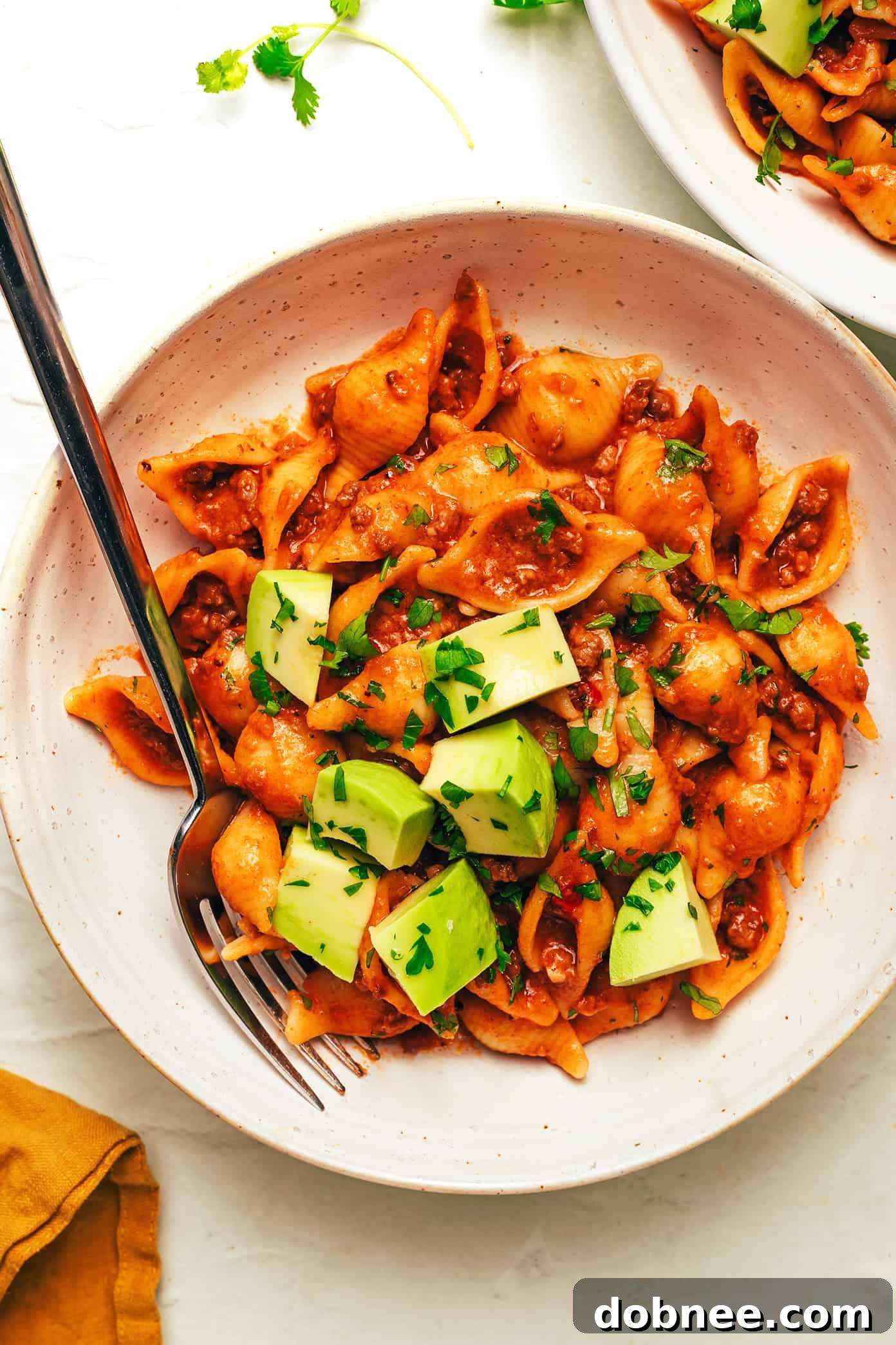 A vibrant close-up of One Pot Cheesy Taco Pasta, showcasing the rich sauce, melted cheese, and ground beef, with pasta shells visible.