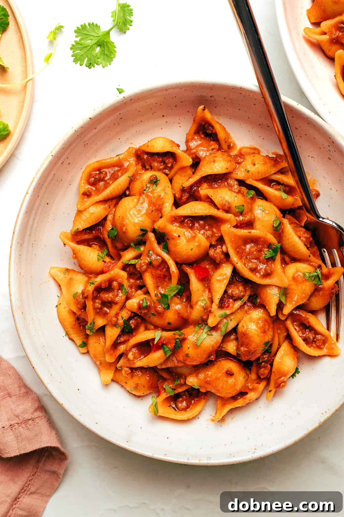A bowl of One Pot Cheesy Taco Pasta, garnished with fresh cilantro and a lime wedge, placed on a wooden surface.