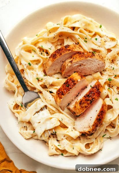 Fettuccine Alfredo with pan-seared chicken, garnished with parsley.