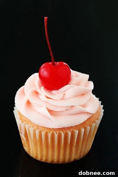 Close-up of freshly baked Cherry Vanilla Cupcakes with smooth pink frosting and a cherry on top, arranged on a cooling rack
