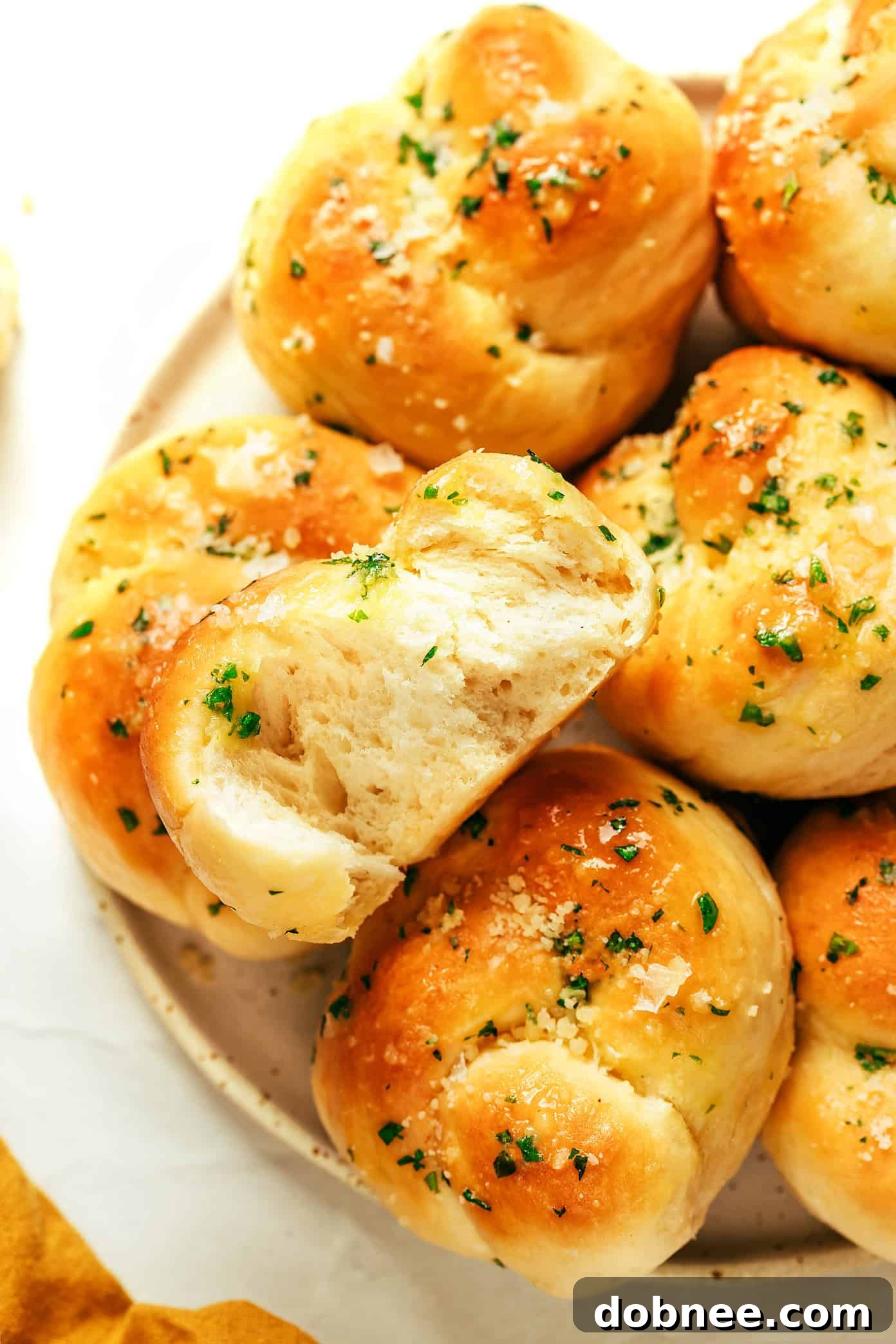 A wide shot of a platter of baked garlic knots, garnished with fresh parsley and Parmesan, ready to serve.
