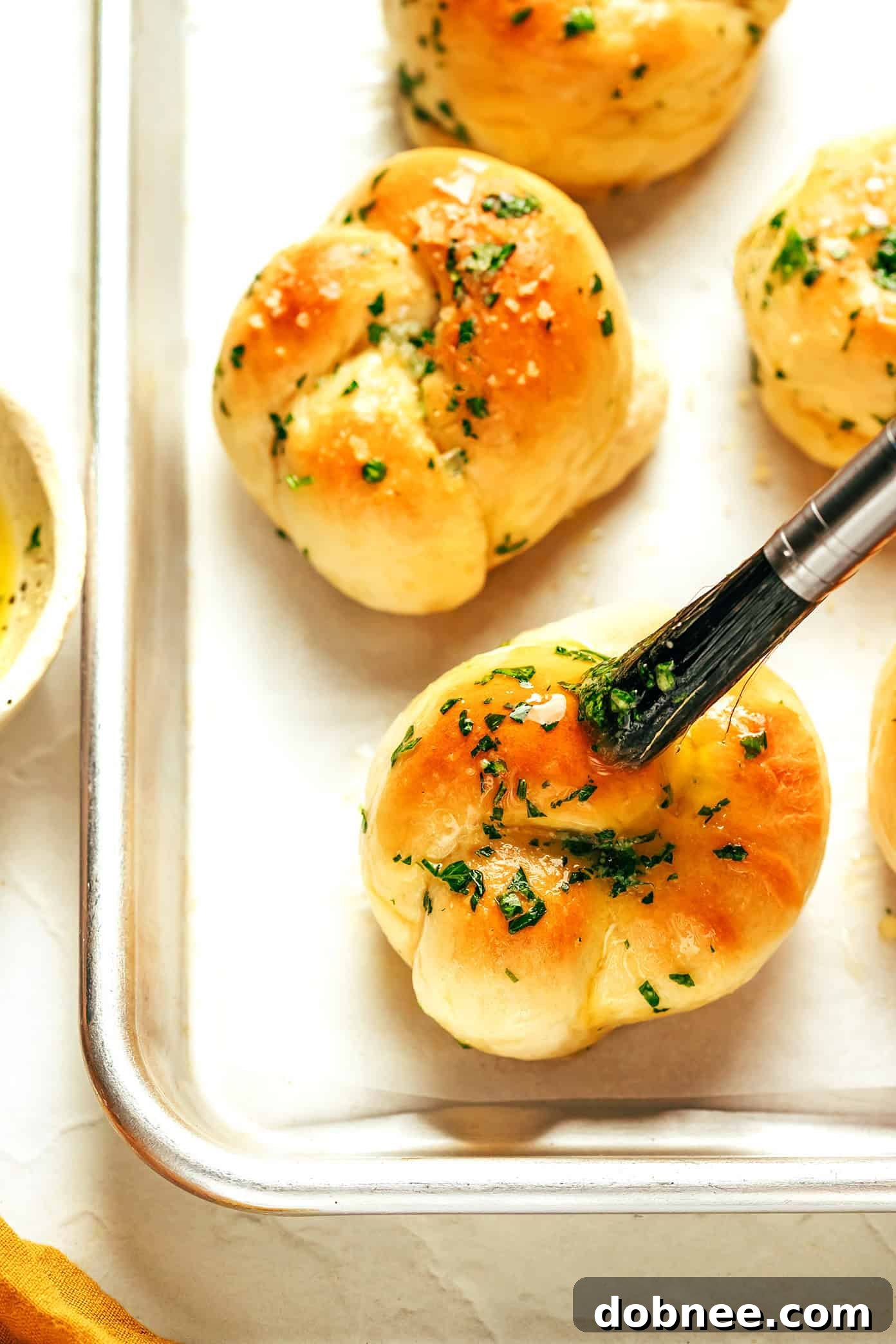 Unbaked garlic knots, carefully tied and arranged on a parchment-lined baking sheet, ready for their final rise.