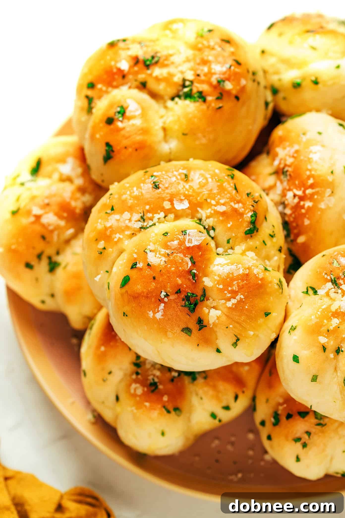 A basket full of freshly baked garlic knots, ready to be served, with a hint of Parmesan and herbs visible.