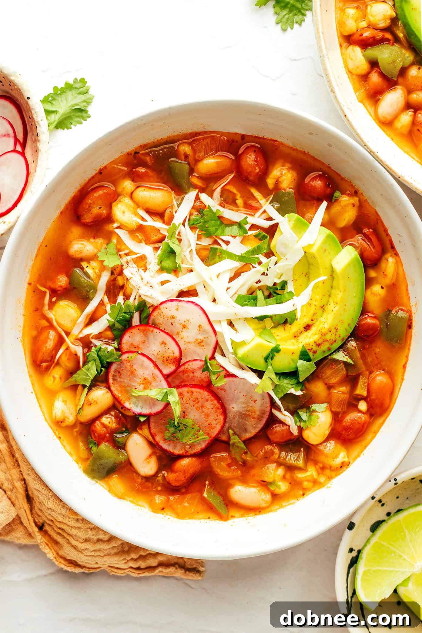 Plant-Powered Pozole 6 Four individual bowls of vegetarian pozole on a white surface, each uniquely garnished.