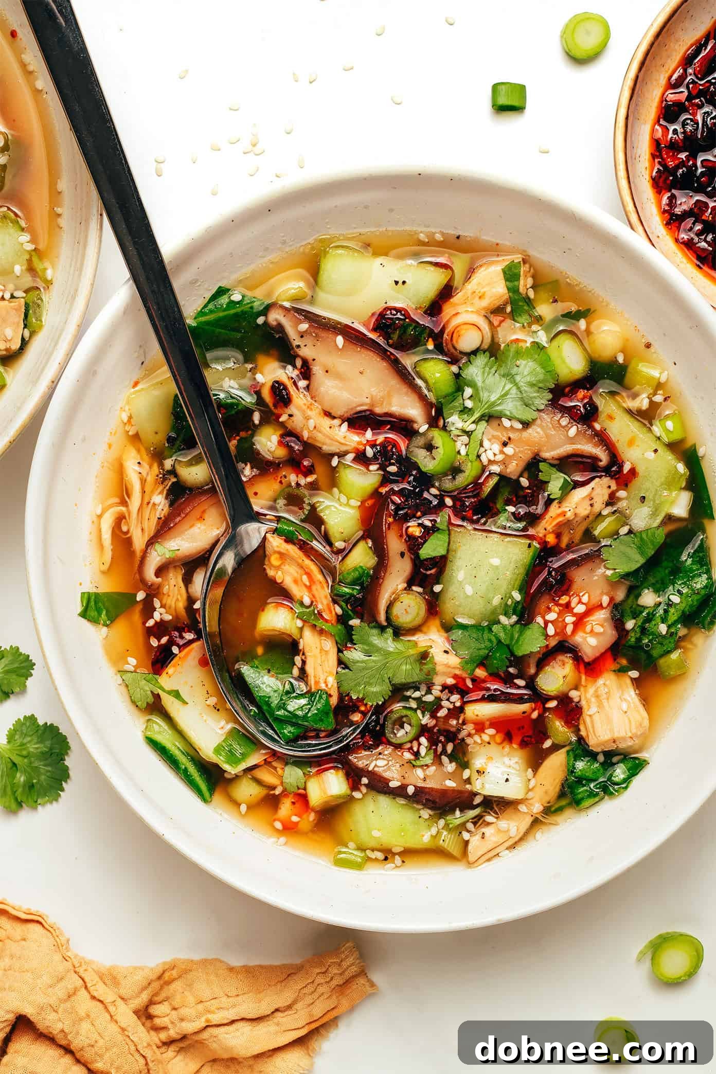 A steaming bowl of ginger scallion chicken soup with fresh herbs.