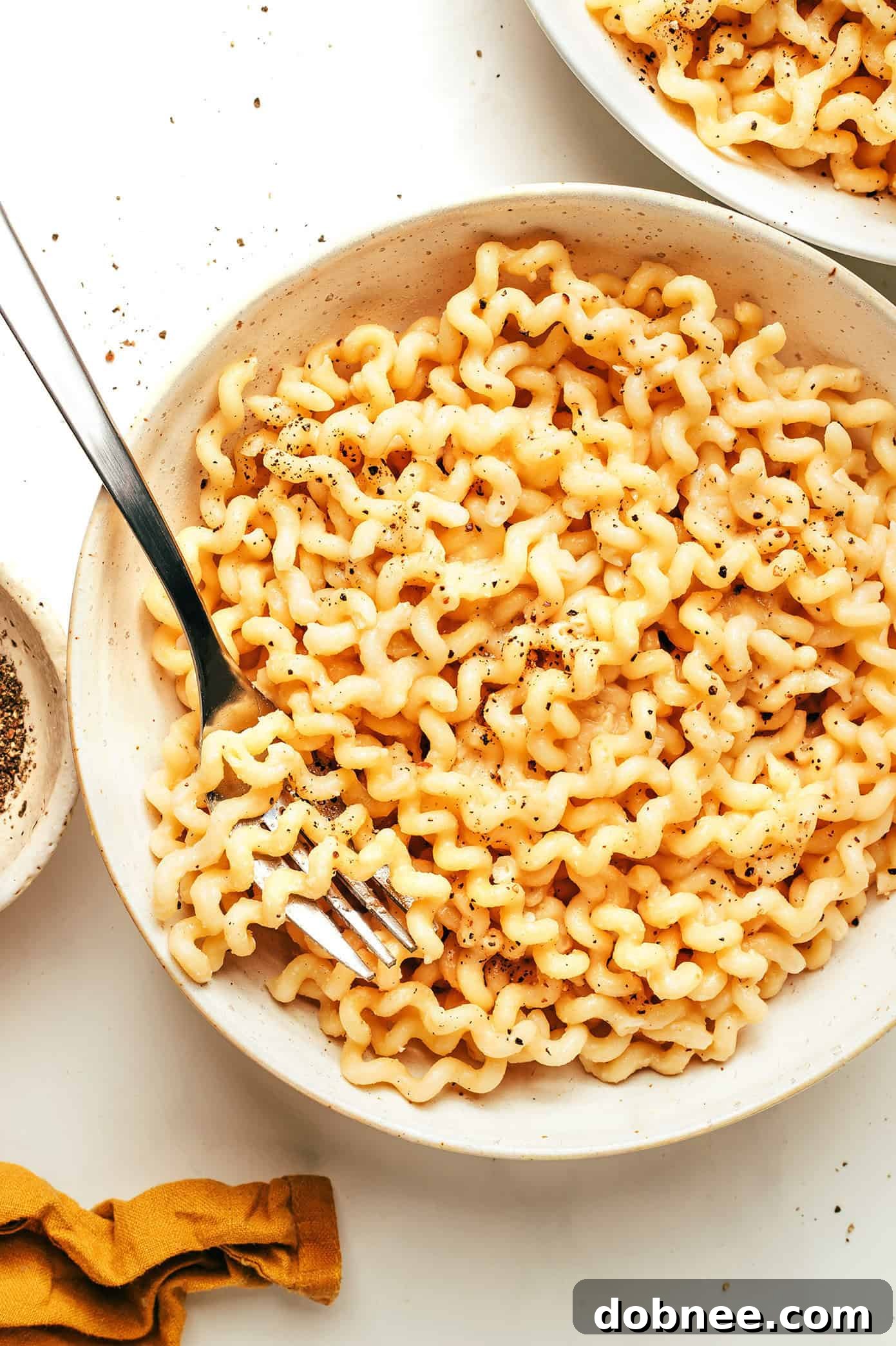 An overhead shot of a large serving bowl filled with garlic miso pasta, garnished with fresh green herbs.