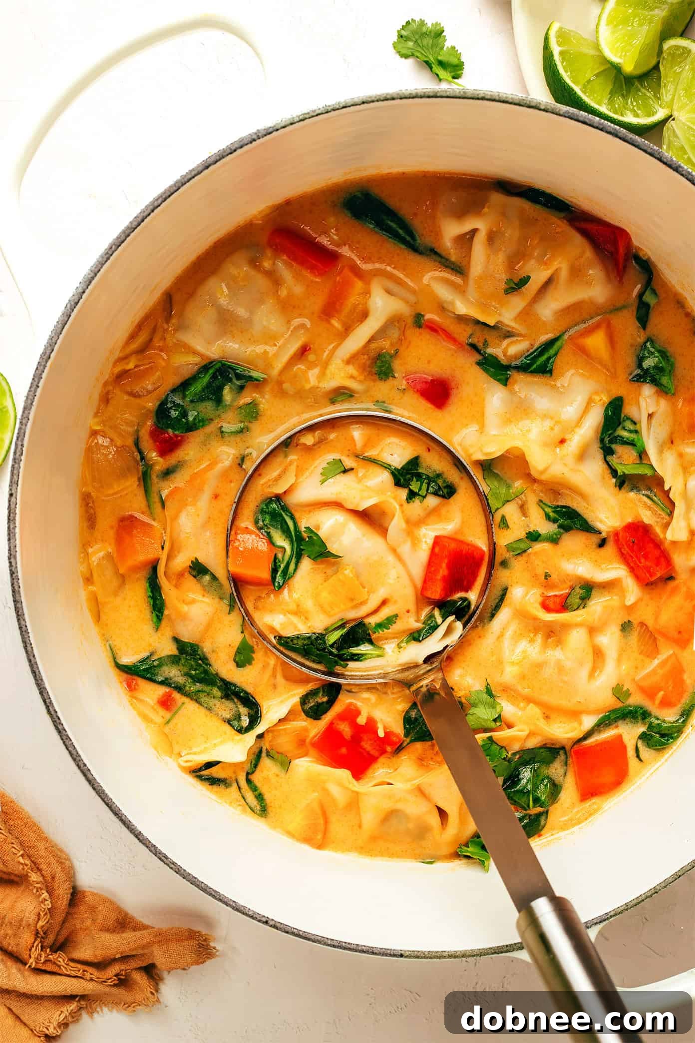 A bowl of vibrant Thai Red Curry Potsticker Soup, garnished with fresh cilantro and lime wedges, steaming gently on a rustic wooden surface next to fresh ingredients.