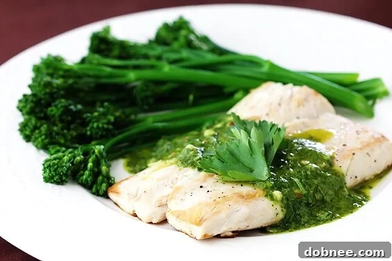 Mahi Mahi with vibrant green chimichurri sauce and tender broccolini on a white plate, ready to be served.