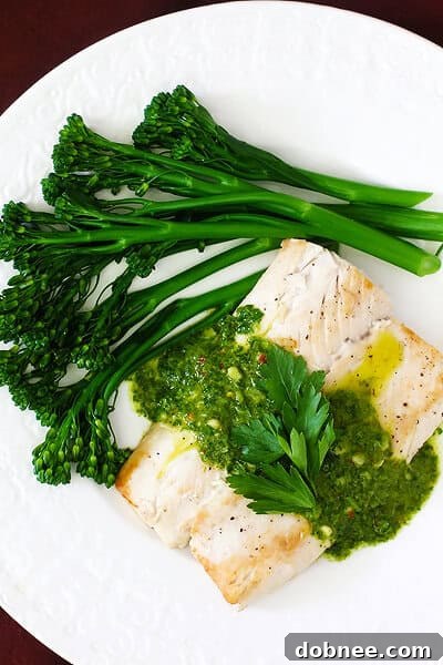 Close-up of a perfectly pan-seared Mahi Mahi fillet drizzled with chimichurri sauce, accompanied by steamed broccolini on a minimalist white plate.
