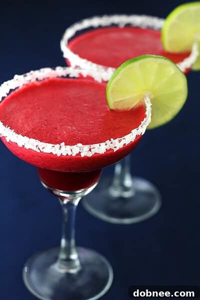 Two glasses of Blackberry Lime Margaritas, one frozen and one on the rocks, garnished with lime and fresh berries.