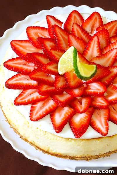 Close-up of a slice of Strawberry Margarita Cheesecake, showing layers of pretzel crust, creamy filling, and lime topping with strawberry garnish.