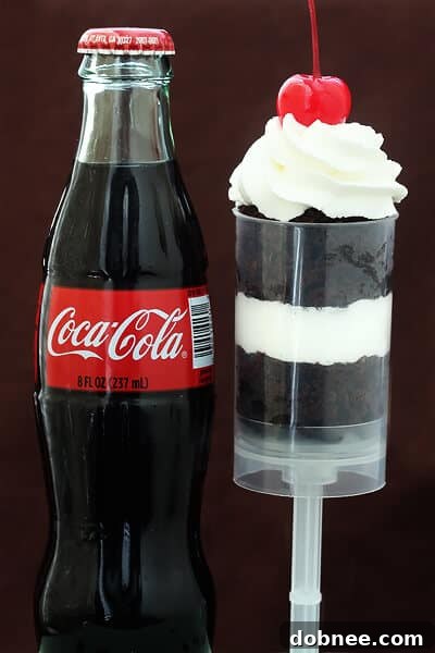 Assembled Coke Float Push-Up Pops, showcasing layers of Coca-Cola chocolate cake, homemade whipped cream, and a maraschino cherry, ready to be served.