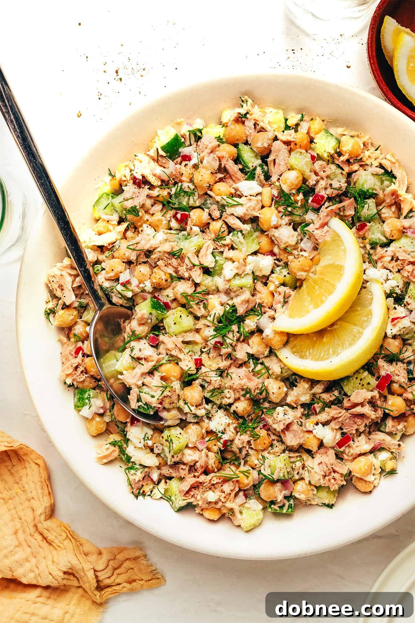 A beautifully arranged chickpea tuna salad in a bowl, garnished with fresh dill and a lemon slice.