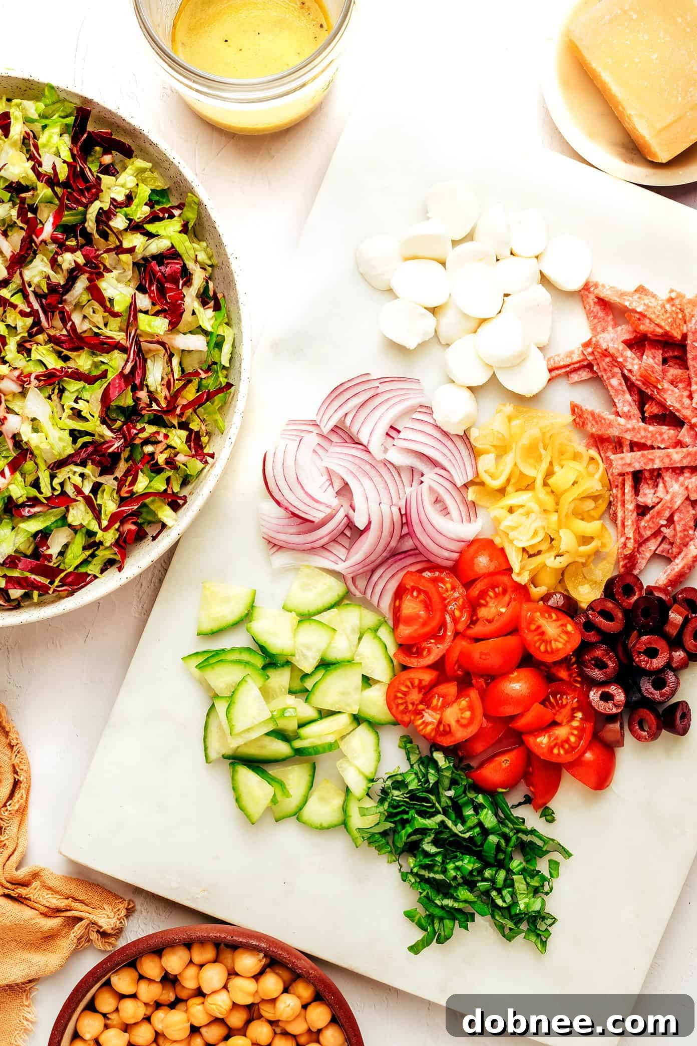 Fresh ingredients for Italian chopped salad including salami, tomatoes, and olives