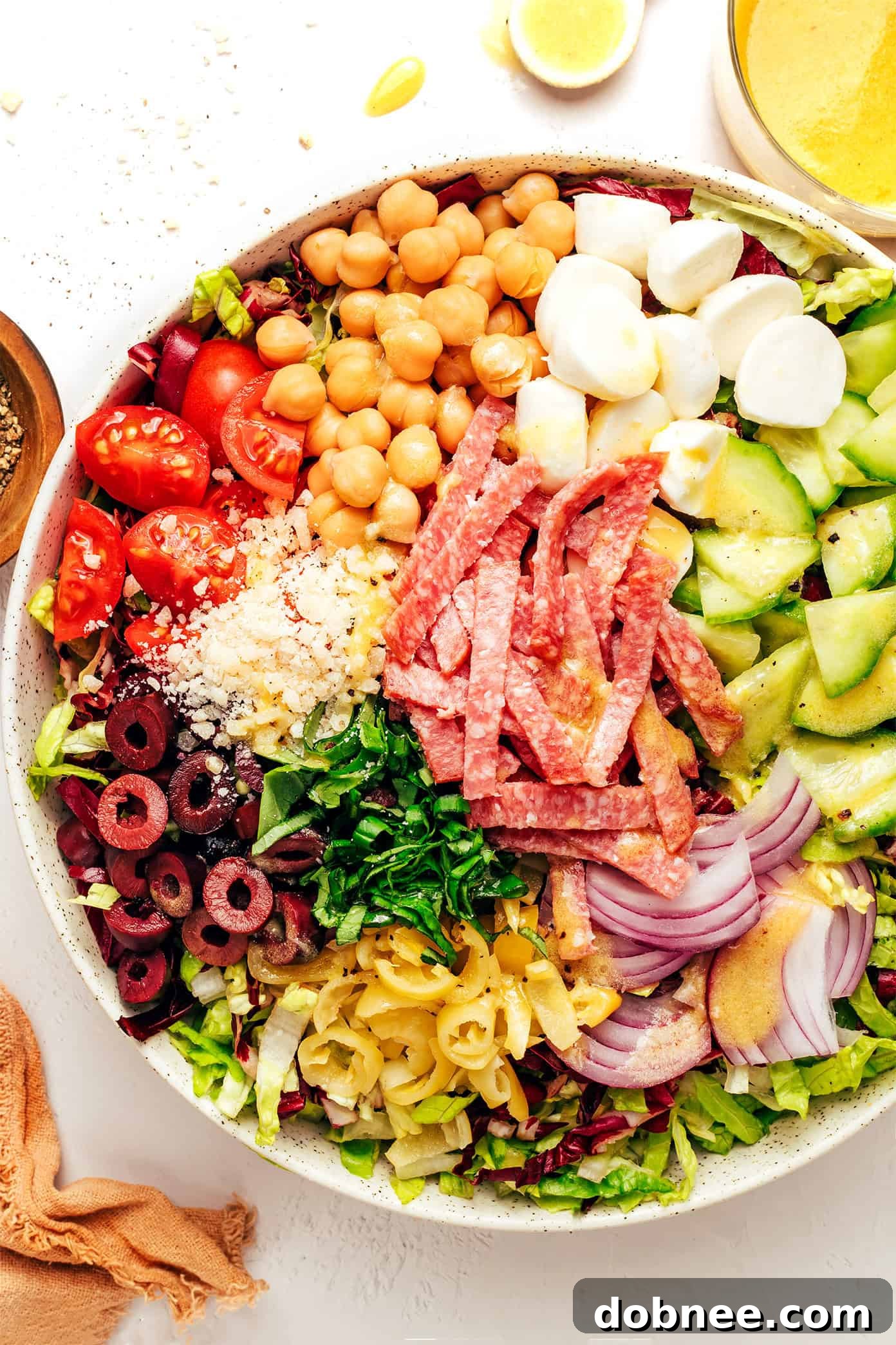 Process of assembling an Italian chopped salad, adding ingredients to a bowl
