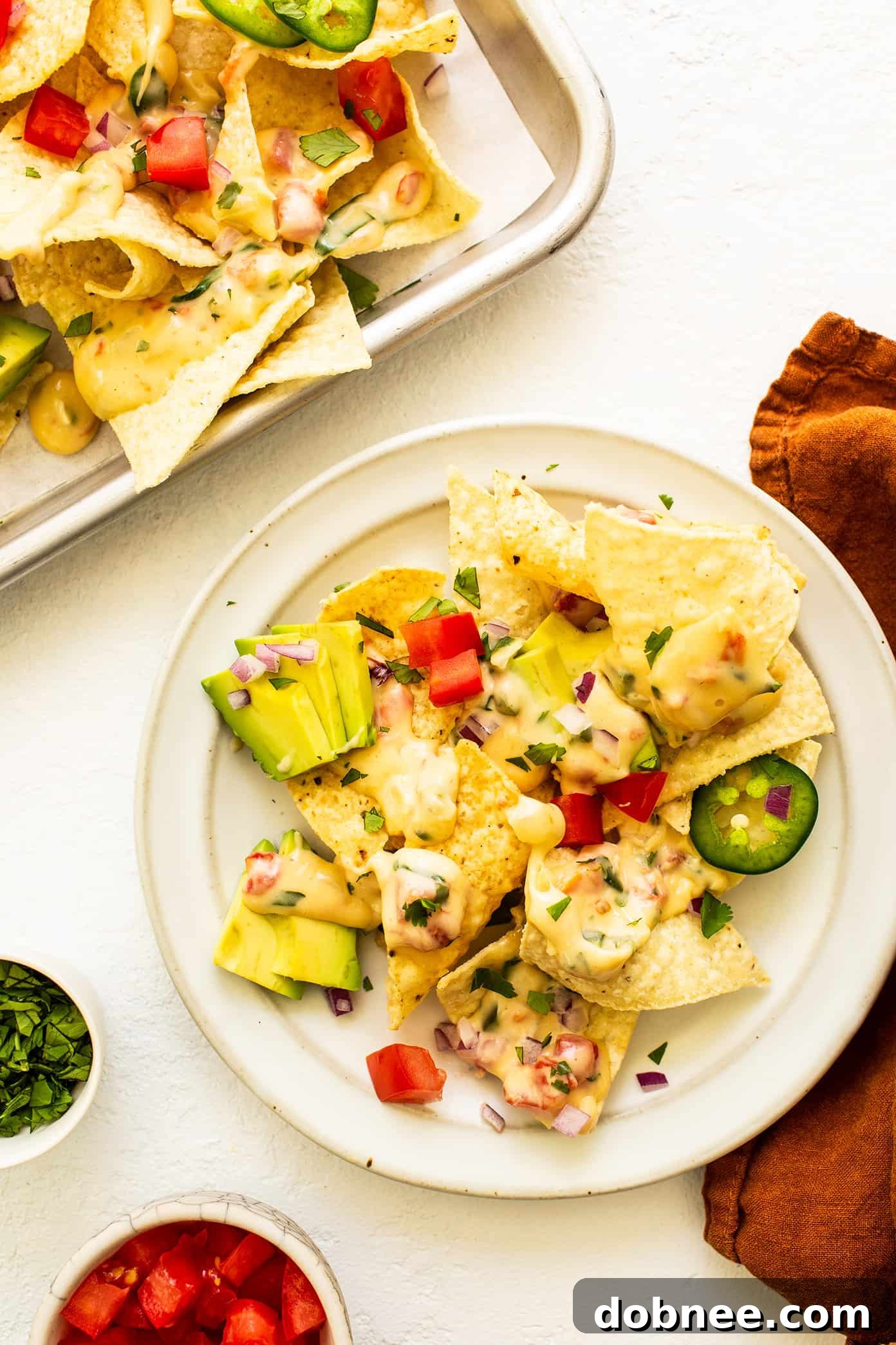 A generous serving of nachos piled high with golden tortilla chips and drenched in creamy Queso Blanco, ready to be enjoyed.