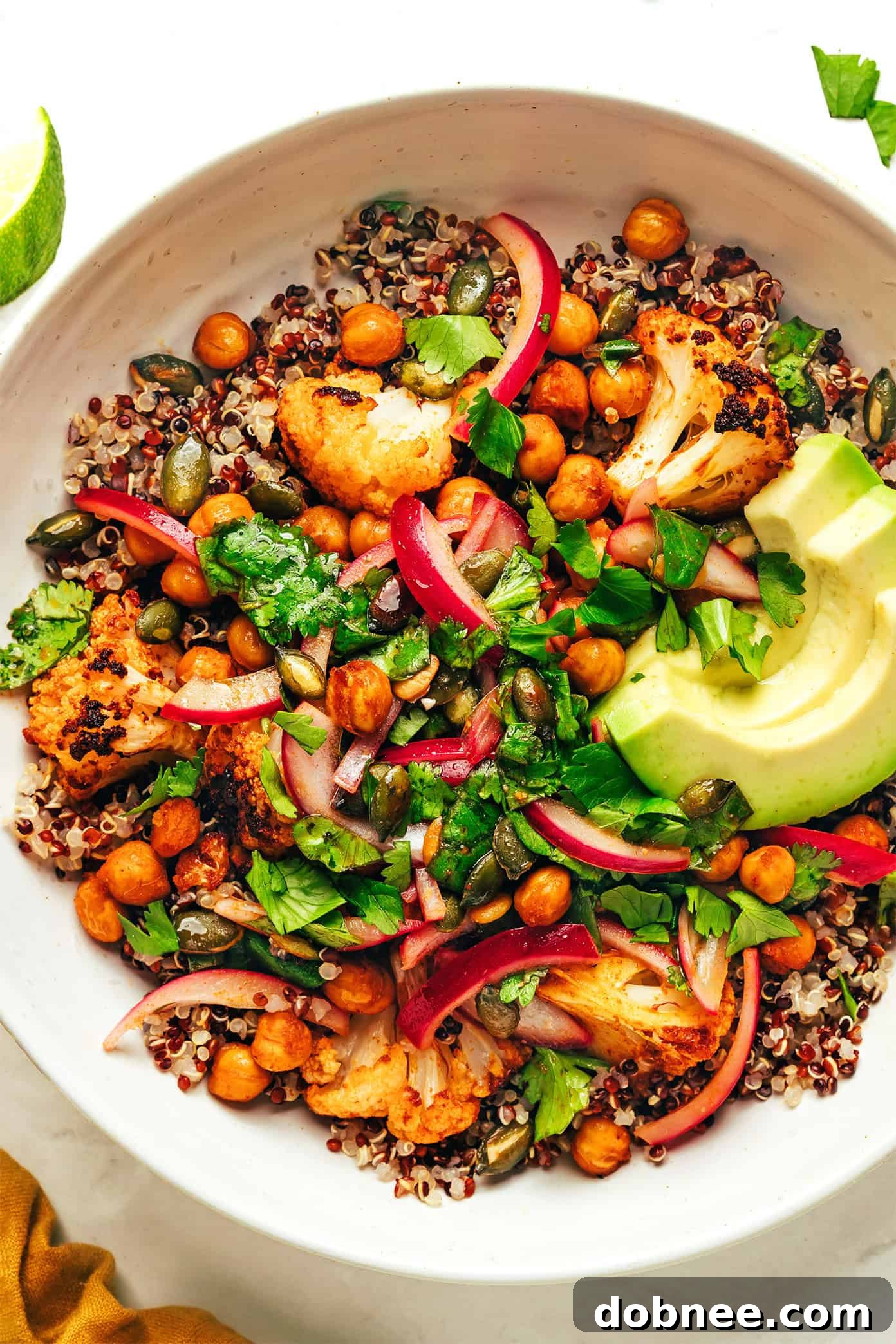 A beautifully plated bowl of chili-lime roasted cauliflower, chickpeas, and quinoa, topped with pickled red onions and avocado.