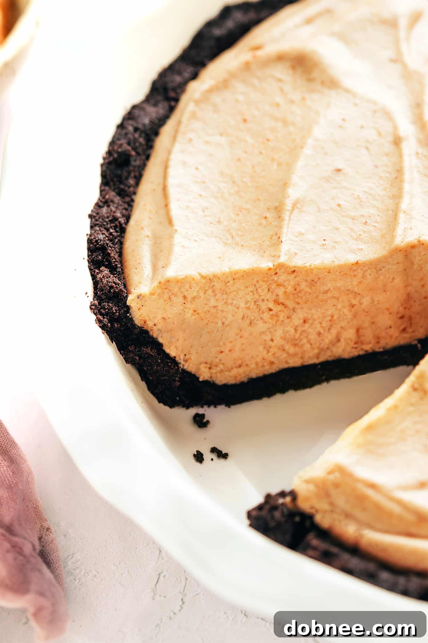 A whole no-bake peanut butter pie with a slice carefully removed, revealing the creamy filling and crunchy Oreo crust, ready for serving.