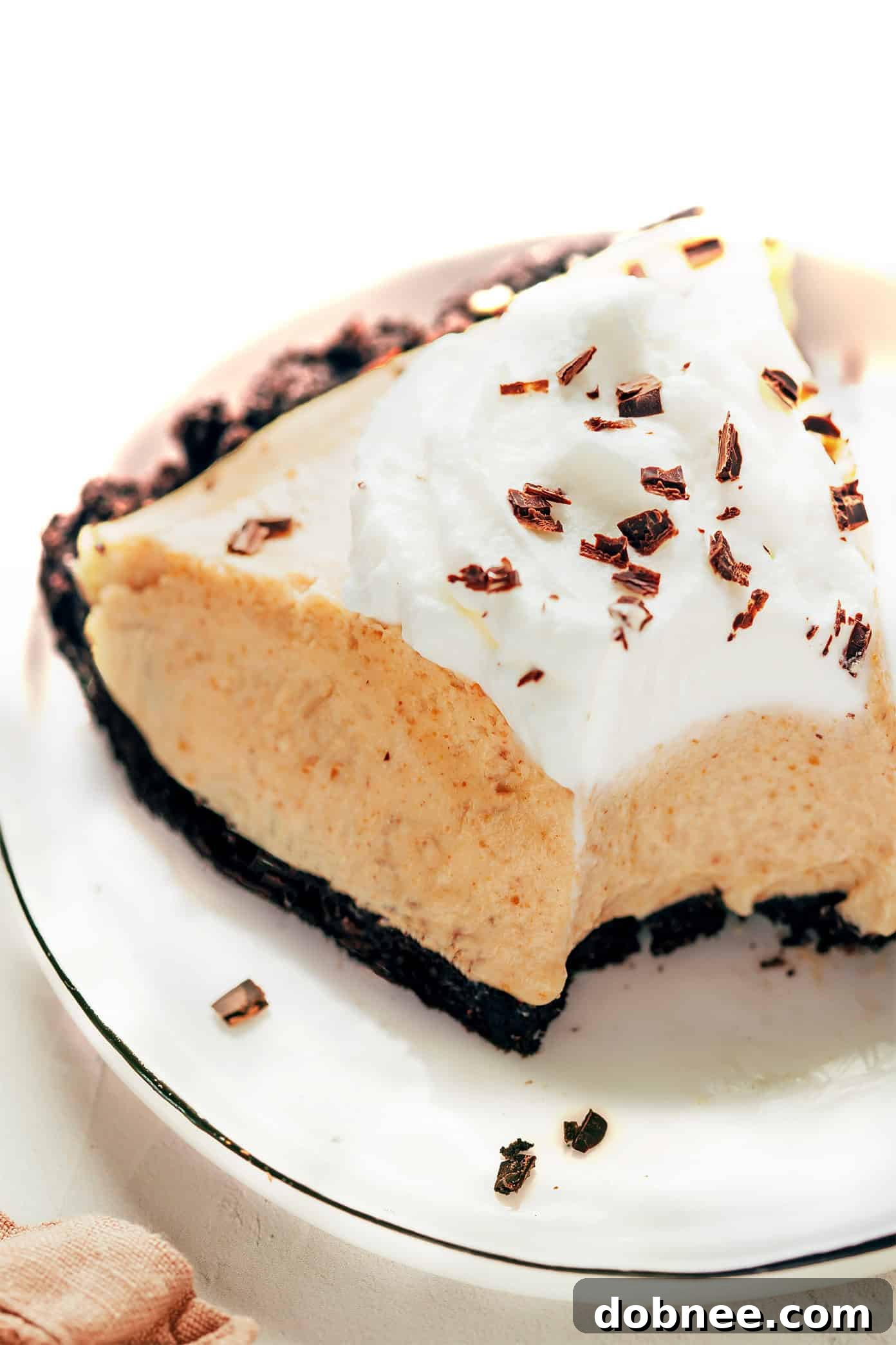 A perfect slice of no-bake peanut butter pie, topped with a generous dollop of whipped cream and chocolate shavings, served on a plate.
