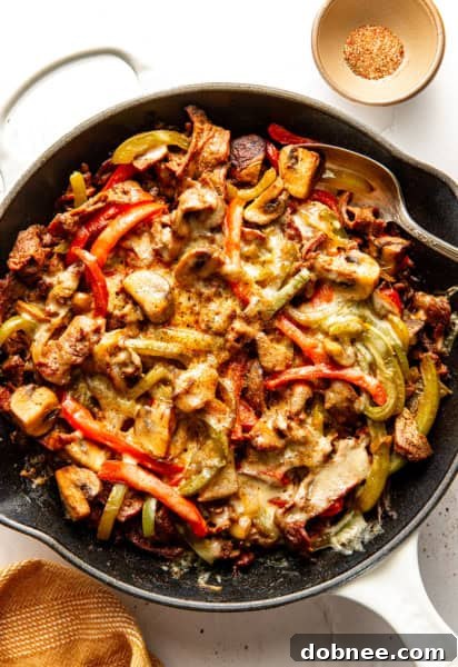 A close-up shot of a steaming Zesty Philly Cheesesteak Skillet, showcasing thinly sliced steak, colorful bell peppers, onions, mushrooms, and melted provolone cheese.