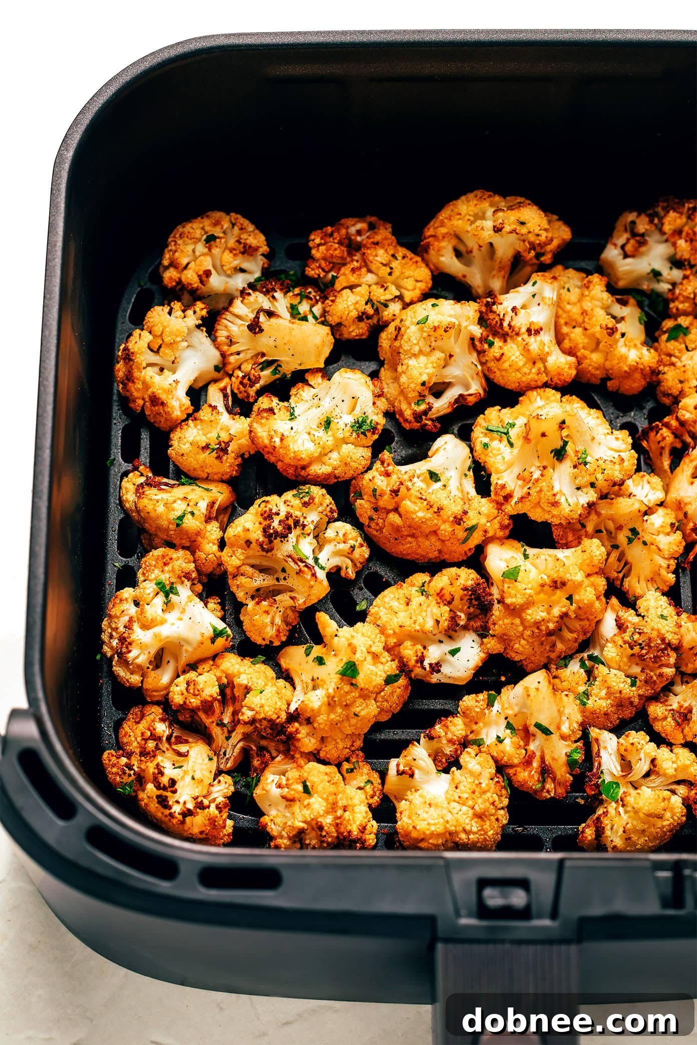 Close-up of crispy air fryer cauliflower florets in a white bowl with a fork.