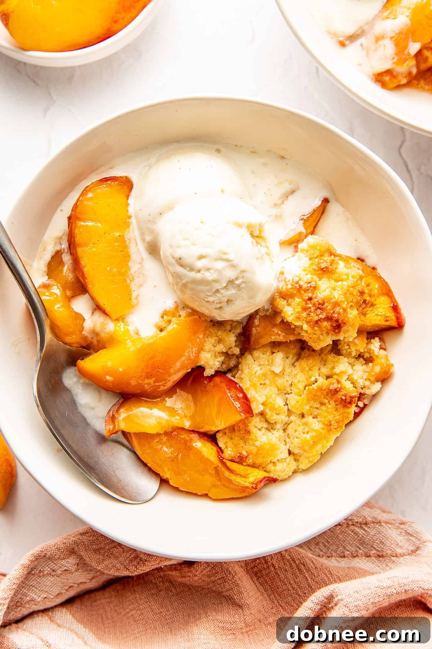A bowl of warm peach cobbler topped with a melting scoop of vanilla ice cream, ready to eat.