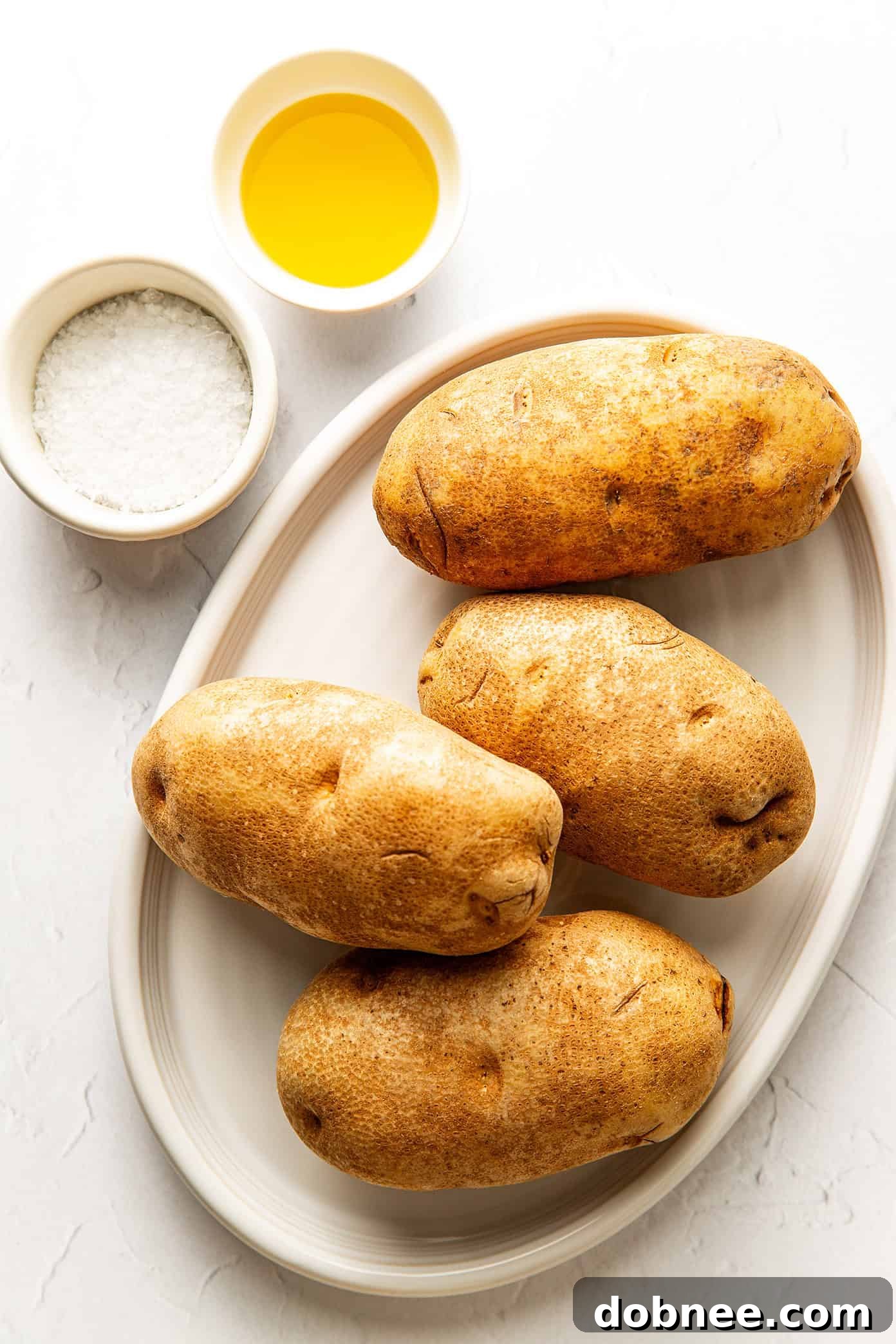 Ingredients for air fryer baked potatoes: Russet potatoes, olive oil, and flaky salt.