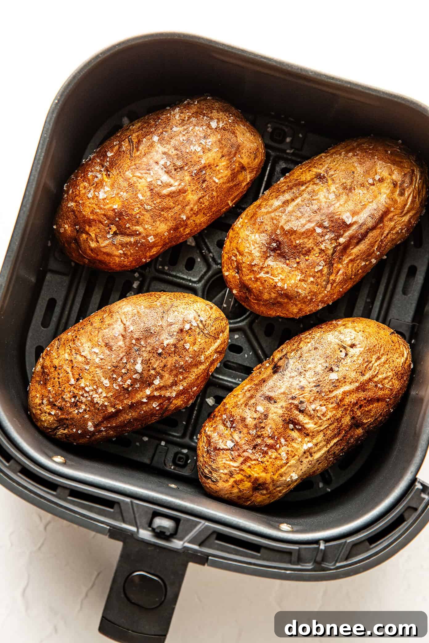 Air fryer baked potatoes sprinkled with flaky sea salt, highlighting their crispy skin.