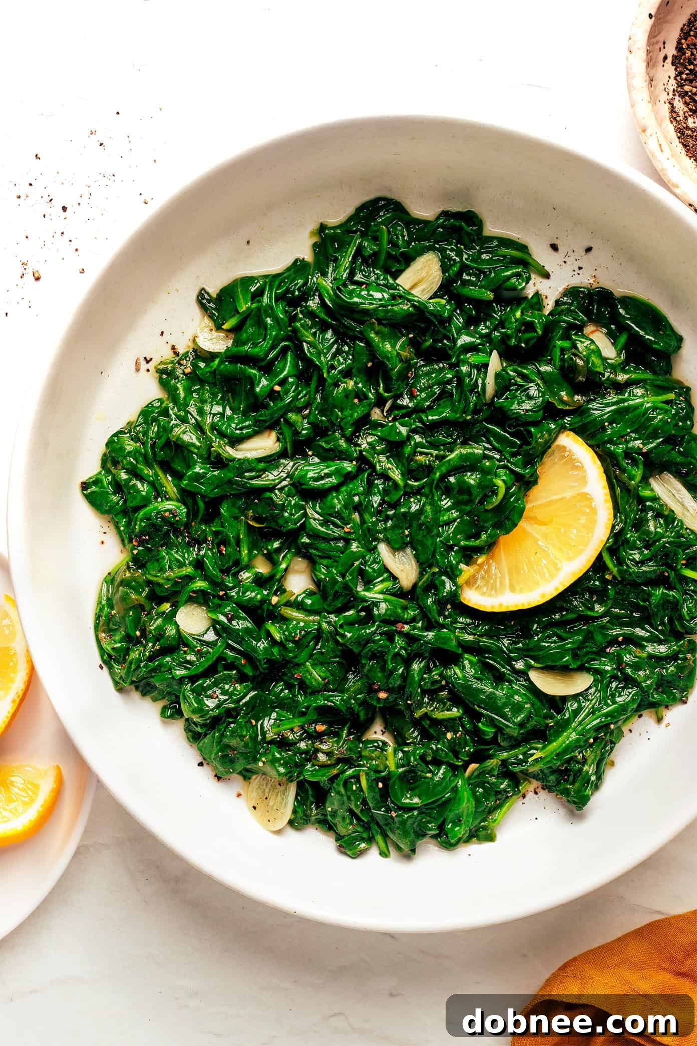 A serving of sautéed spinach garnished with a lemon wedge, ready to eat