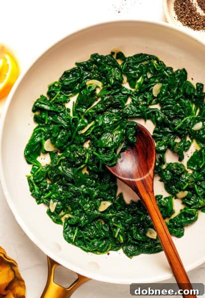 A plate of sautéed spinach with a lemon slice and a fork