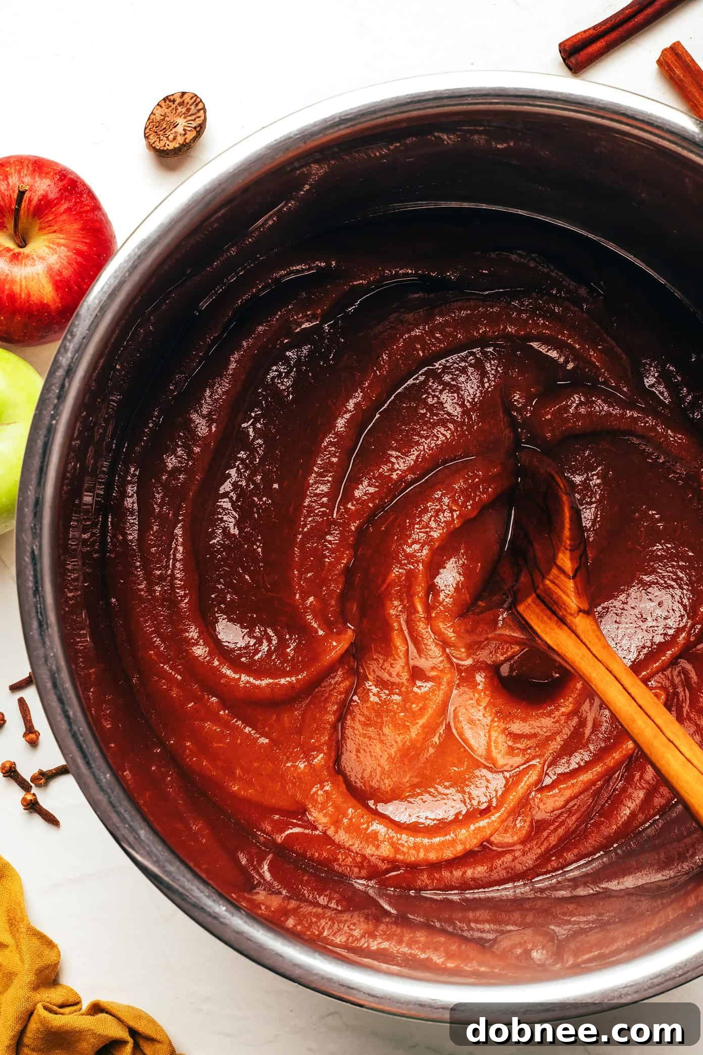 Freshly made apple butter in jars, with apples and spices around.