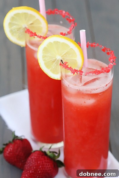 A refreshing glass of Sparkling Strawberry Lemonade, rimmed with popping candy, garnished with fresh strawberries and lemon slices.