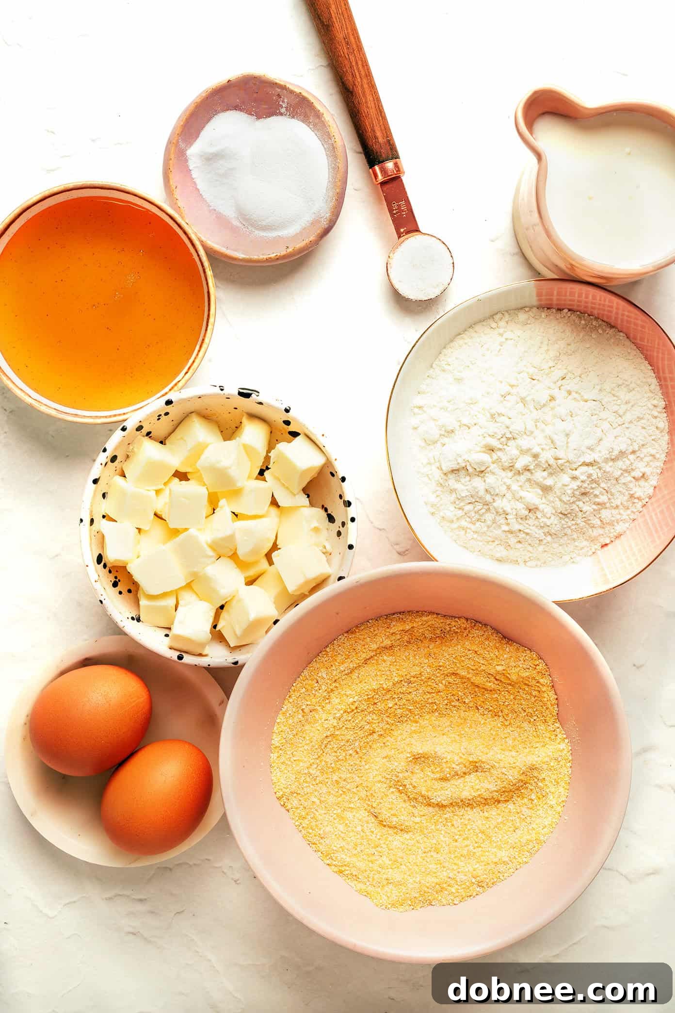 All the essential ingredients for making honey cornbread muffins laid out on a table.