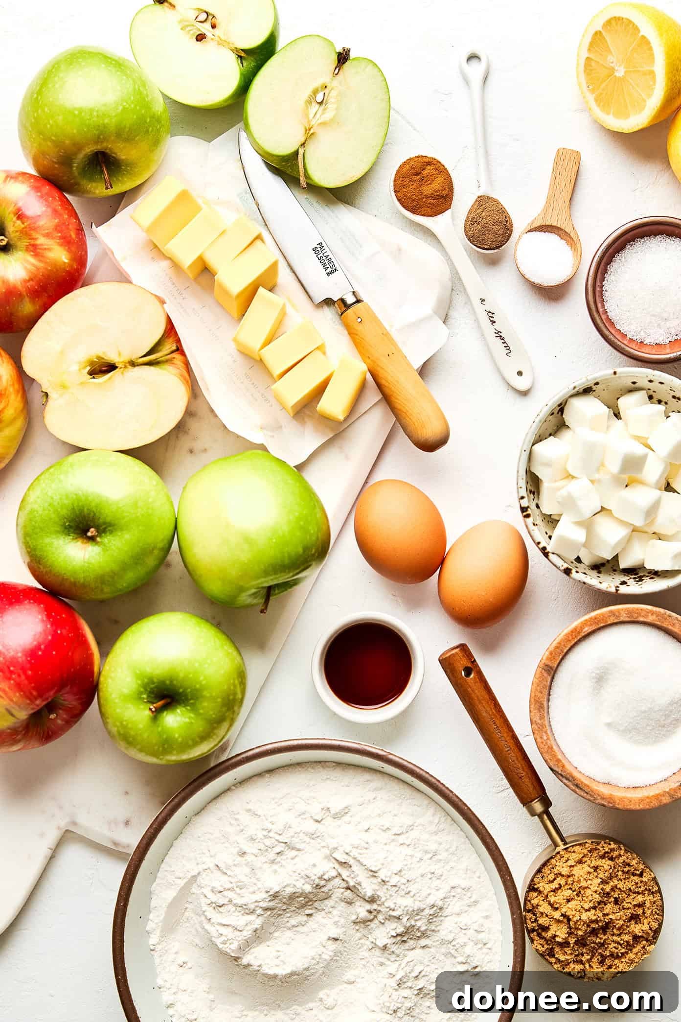 A flat lay photograph showcasing all the fresh ingredients needed to bake a homemade apple pie, including apples, flour, butter, and spices.