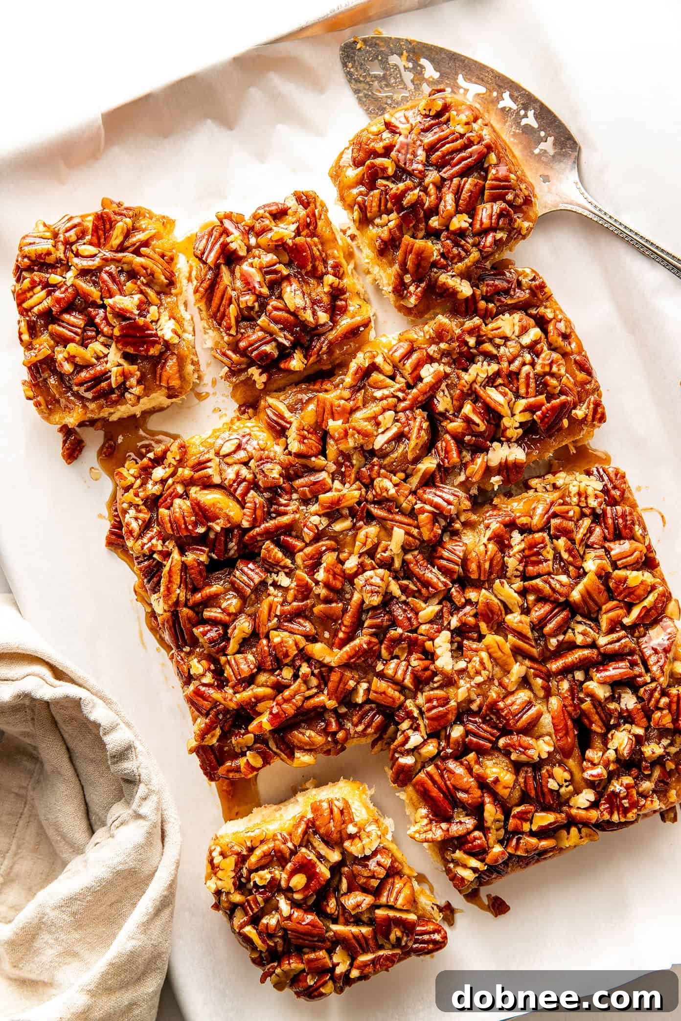 A single maple pecan sticky bun with its gooey caramel and pecan topping, delicately pulled apart to show the soft, swirled interior