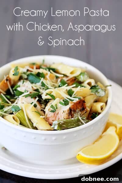 Overhead view of a large pan filled with Lemon Rosemary Pasta, featuring golden chicken, green asparagus, and wilted spinach, ready to be served.
