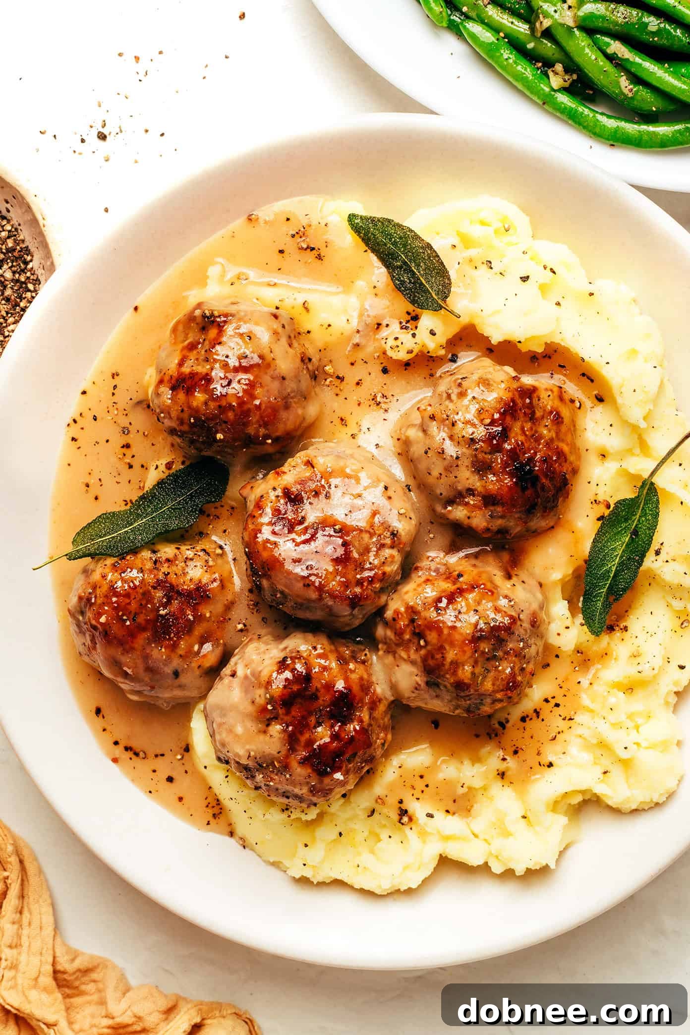 A plate of juicy turkey meatballs smothered in rich, herb-infused gravy, garnished with fresh sage.