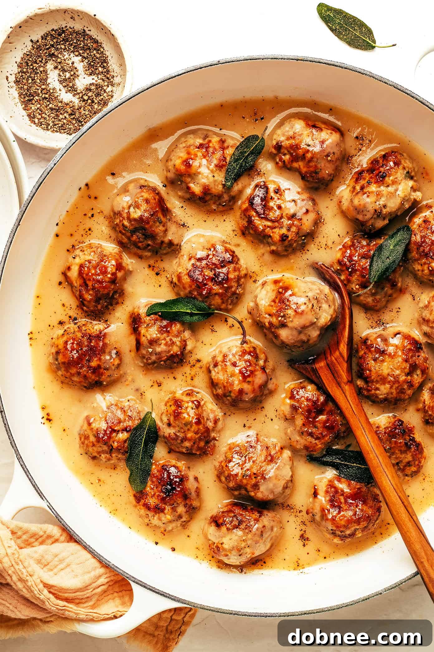 A close-up of a single turkey meatball, perfectly browned, garnished with fresh sage.